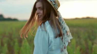 Güneş ışığında şapka takan çekici bir kadın kameraya bakıyor. Sıcak doğa tatili. Yavaş çekimde genç bir portre.