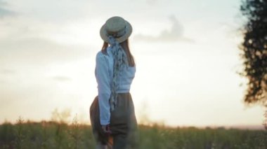 Güneş ışığında yürürken şapkalı mutlu bir genç kadın etrafına bakıyor sıcak doğa tatilleri yavaş çekimde genç portreler.