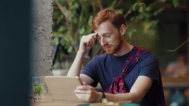 Kafede sosyal medyada dijital tablet bilgisayar kullanan yalnız kızıl saçlı yakışıklı adam. Şık bir iç mekan. İletişim cihazı. İş adamı.