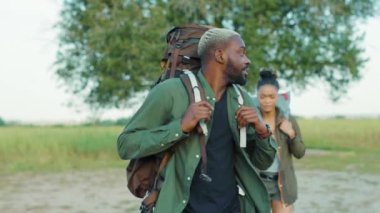 Turist sırt çantalı birkaç güzel Afro-Amerikalı Afrika savanasında el ele yürüyüp balayı tatilinin tadını çıkarıyorlar..