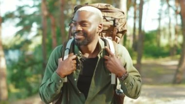 Afro-Amerikalı yürüyüşçü, turist sırt çantalı yakışıklı adam kameraya gülümseyerek tek başına seyahat ediyor. Pozitif siyah turist vahşi doğayı keşfediyor.