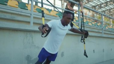 NEW YORK - 5 Eylül 2020: Trx fitness ipi ile çalışan Afro-Amerikan genç adamı stadyum kas antrenmanlarında spor kıyafetleri spor antrenmanlarında antreman yapıyor.