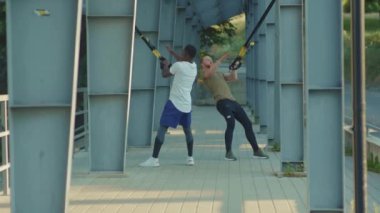 NEW YORK - 5 Eylül 2020: Güneşli bir günde yakışıklı iki adam birlikte spor spor giyim spor kıyafetleri için stadyum Afrika kökenli Amerikan spor giyim sporu antrenmanlarında trx fitness ipi ile vücut egzersizleri yapıyorlar.