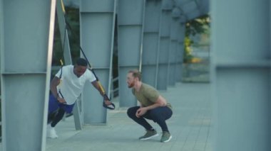 NEW YORK - 5 Eylül 2020: Sportif genç adam, başka bir Afrikalı Amerikalıyı spor kıyafetleri spor antrenmanlarında trx fitness halatıyla dışarıda vücut egzersizleriyle motive etti