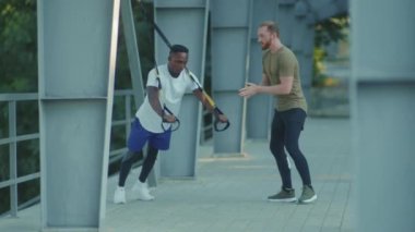 NEW YORK - 5 Eylül 2020: Birbirlerini motive eden iki genç adam, Afro-amerikalı bir adamı, dışarıda trx fitness halatıyla vücut egzersizleriyle stadyum kaslı spor kıyafetleri spor antrenmanlarında motive etti.