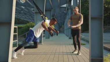 NEW YORK - 5 Eylül 2020: Yakışıklı genç adam, başka bir Afrikalı Amerikalıyı spor kıyafetleri spor antrenmanlarında trx fitness halatıyla dışarıda vücut egzersizleriyle motive etti
