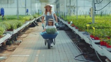 El arabası çiçekli komik kızı olan komik mutlu anne kadın yaz yeşili ailede serada kamera tebessümüne bakar kadın çocuk doğası açık hava çocukluğu ağır çekim