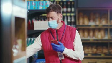 Maskeli genç satıcı markette telefon kullanıyor. Avokado karantinada. Sebze işinde.