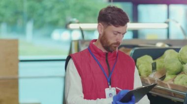 Genç satıcının portresi süpermarkette deftere yazıyor. Kamera, sebze, güzel, taze ürünler, perakende, yavaş çekim.