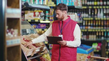 Ciddi genç satıcı defterine bir şeyler yaz. Süpermarkette sebze işi. Güzel, taze, perakende satış mağazası.