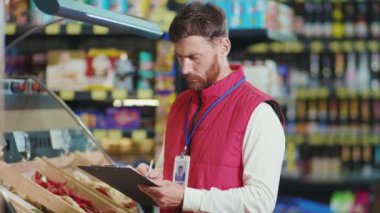 Yakışıklı genç satıcı, süpermarkette çek yazar. Sebze işi. Güzel, taze, perakende satış mağazası.