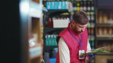 Kapalı gişe oynayan genç adam sebzeleri süpermarketin raflarına koyuyor sebzeleri kontrol ediyor güzel, taze, perakende satış yapan, yavaş çekim yapan bir dükkan.