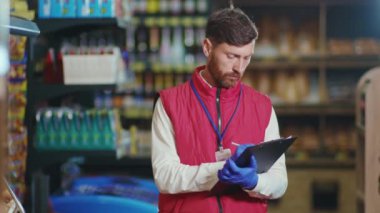 Genç satıcının portresi süpermarkette deftere yazıyor. Kameraya bak. Ciddi sebze işi.