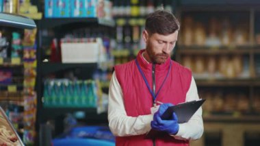 Kapalı gişe genç satıcı süpermarkette deftere bir şeyler yazıyor. Kameraya bak. Ciddi sebze işi. Güzel, taze, perakende satış mağazası.