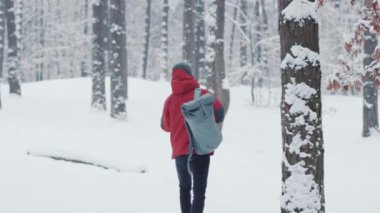 Sırt çantalı sakallı genç adam, kış ormanlarında yürüyor, konuşuyor, gülümsüyor, gezgin, gezgin, gezgin, gezgin, gezgin, kar turizmi, dağ iletişim ormanı, açık hava aktivitesi, soğuk, yavaş çekim.