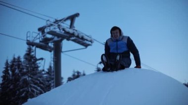 Komik gülümseyen genç adam tepeden kayıyor yüzü kıpkırmızı soğuk kış gününden dağlarda insanlar dışarıda kar yağışı yapıyor çocuk.