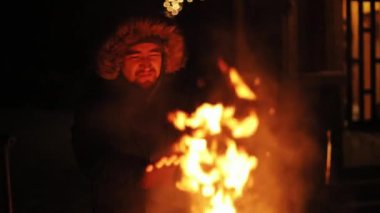 Portre gülümseyen genç adam sıcak eller açık bir şömine gece mutlu kış dağları yakacak odun odun kara doğa duman sıcak turuncu kamp akşamı vahşi soğuk yolculuk yavaş hareket