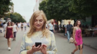 Güzel bir kadın şehir merkezinde telefon yürüyüşü yapıyor. Gülümse. Mutlu bir yaz internet işi.