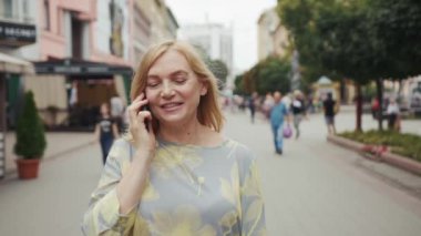 Gülümseyen orta yaşlı sarışın kadın telefonda konuşurken sokak şehri modern akıllı telefon teknolojisi meşgul iletişim özgüveni ile bağlantılı portre yakın çekim