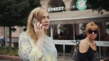Ciddi orta yaşlı sarışın kadın telefon kulübesinde konuşuyor modern akıllı telefon teknolojisi iletişim özgüven portresiyle meşgul.