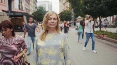 Orta yaşlı sarışın kadın kameraya bakıyor. Şehir merkezinde gülümsüyor. Son sınıf, çekici, dış görünüşü güzel.