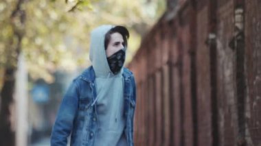 Kar maskeli, kimliği belirsiz genç adam duvarın yanında duruyor ve elinde sprey boya tutuyor. Vandalizm, sokak sanatı, hobi. Banliyö bölgesi, eğlence, isyan, protesto. Görüntüyü kapat