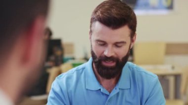 Neşeli sakallı bir adamın banka asistanıyla iletişim kurması, sorular sorması, olumlu kafa sallaması. Anlaşma, sözleşme, bilgi. Karar verme, imza, finans