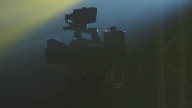 Koyu arkaplanda projektörün parıldayan ışığında profesyonel dijital video televizyon kamerasının yakın görüntüsü. Televizyon stüdyosu, çekim, çekim. Meslek konsepti, teknik