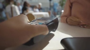 Erkek veznedar müşteri için postu masaya yerleştiriyor. Kafedeki banka terminalini kullanarak kredi kartı NFC teknolojisiyle ödeme yapan genç bir kadın..