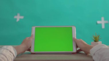 Yeşil arka plandaki ahşap masada yeşil ekran maketine sahip tablet, modern yatay aygıt kullanan yakın plan kızı.