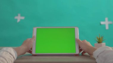 Çalışma masasındaki yeşil ekranlı tablet portatif yatay bilgisayarda yeşil arka planda sosyal ağa göz atan genç bir kadın..