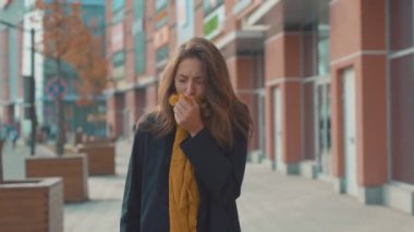 Üzgün genç bir kadın kameraya bakıyor. Açık havada ateş, soğuk alerji, şehir güzel hastalık, kadın burun hapşırması, akıcı doku, hava kirliliği, yetişkin hastalıkları bölgesi ağır çekim