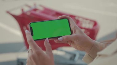 NEW YORK - 19 Mayıs 2019: Elinde yeşil ekranlı yatay telefonu olan ellerini kapatan kadın süpermarket yakınlarındaki arka plan arabasında internet teknolojisi akıllı telefonu araklıyor.