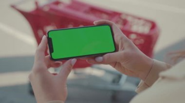 NEW YORK - 19 Mayıs 2019: Genç kadın elinde yeşil ekranlı yatay telefonu süpermarket yakınlarındaki arka plan arabasında kullanıyor ve internet teknolojisi akıllı telefonu araklıyor.