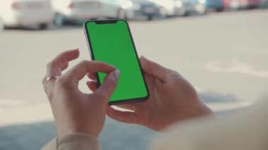 NEW YORK - 19 Mayıs 2019: Güneşli bir günde elinde yeşil ekran ile dikey telefon tutan genç kadın, internet teknolojisi akıllı telefon mesajı cep telefonu mesajlarını araklıyor.