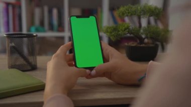 NEW YORK - 19 Mayıs 2019: Home Sitting on Chair 'de oturan bir kadının cep telefonu ya da akıllı telefonunun dikey yeşil ekranlı görüntüsü. Chroma Anahtar Akıllı Telefon Teknolojisi. Cep Telefonu Evi