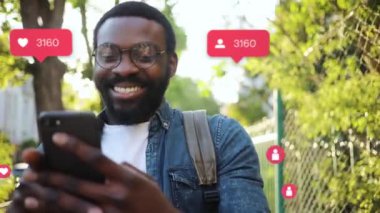 NEW YORK - 19 Mayıs 2019: Gözlüklü çekici Afrikalı Amerikalı adam gülümseyen mutlu vlogger etkisi yaratıcı animasyonu kullanıcı arayüzü - beğeni, takipçiler, akıllı telefondan sosyal medya yorumları