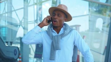 Şapka standındaki Afro-Amerikan yüzünü kapat ve havaalanı yakınlarında telefonla konuş. Tatil ve seyahat. Sohbet başarılı bir açık hava stili gezisi. Kapatın. Yavaş çekim