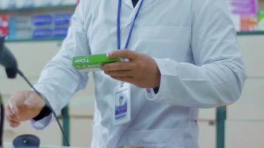 Eczanede çalışan Asyalı eczane uzmanı ilaç reçetesini okuyor ve bilgisayar ekranında fiyatını kontrol ediyor. Melez insanlar. Meslek, sağlık sigortası, sağlık kavramı.