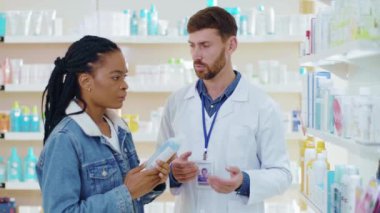 Afrika kökenli Amerikalı bir kadın eczacı erkeğe danışmanlık yapıyor, sağlık ilaçlarını tartışıyor ve eczanedeki güzel yüz derisi ürünlerini inceliyor..