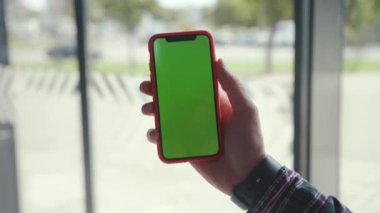 NEW YORK - 5 Nisan 2018: Erkek elinde yeşil krom tuş akıllı telefon. Güneşli bir günde modern cep telefonu kullanan meşgul bir genç..