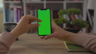 NEW YORK - 19 Mayıs 2019: Home Sitting on Chair 'de oturan bir kadının cep telefonu ya da akıllı telefonunun dikey yeşil ekranlı görüntüsü. Chroma Anahtar Akıllı Telefon Teknolojisi. Cep Telefonu Evi