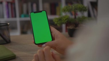 NEW YORK - 19 Mayıs 2019: Home Sitting on Chair 'de oturan bir kadının cep telefonu ya da akıllı telefonunun dikey yeşil ekranlı görüntüsü. Chroma Anahtar Akıllı Telefon Teknolojisi. Cep Telefonu Evi