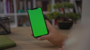 NEW YORK - 19 Mayıs 2019: Home Sitting on Chair 'de oturan bir kadının cep telefonu ya da akıllı telefonunun dikey yeşil ekranlı görüntüsü. Chroma Anahtar Akıllı Telefon Teknolojisi. Cep Telefonu Evi