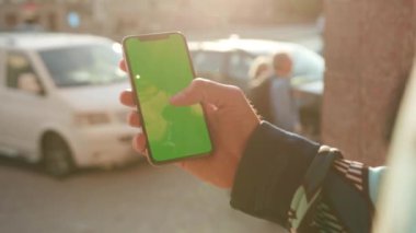 NEW YORK - 19 Mayıs 2019: Güneş ışığı üzerinde dikey yeşil ekranlı telefon kullanan genç adamı kapat arka plan bulanık internet krom dış cep telefonu izolasyon mesajı akıllı kayan telefon