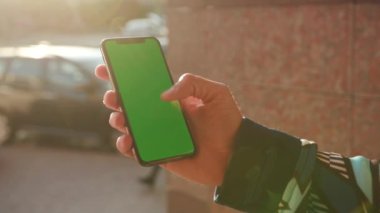 NEW YORK - 19 Mayıs 2019: Güneş ışığı üzerinde dikey yeşil ekranlı telefon kullanan genç adam arka plan bulanık internet krom dış cep telefonu izolasyon mesajı akıllı kayan akıllı telefon