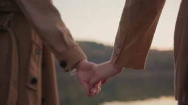 Güzel kadınların elleri arka planda sıkı sıkı ayrılıyorlar. Yakın plan lezbiyen kızlar gün batımında göl kenarında el ele tutuşuyorlar. Aşk ve ilişki kavramı.