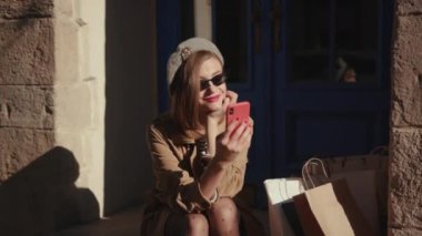 Parlak bir güneş ışığı altında şık bir ceket giyen çekici genç bir kadın şehir merkezinde oturmuş telefon kullanıyor. Gülümsüyor, yaz mevsiminde internet sektöründe ve teknolojinin dışında ağır çekimde gülümsüyor.