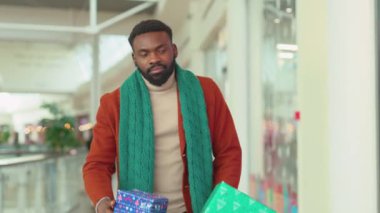 Ciddi Afro-Amerikan genç çekici bir adam Noel hediyeleriyle yürüyor. Kutularda yakışıklı, mutlu alışveriş kutuları. Etrafına bak.