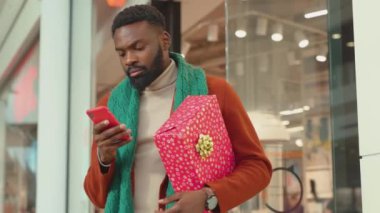 Noel hediyesi olan Afrikalı genç bir Amerikalı 'yı kapatın. Telefonla alışveriş merkezindeki alışveriş merkezindeki internet portresi mobil programcı teknolojisi yavaş çekim hücresine bakın.